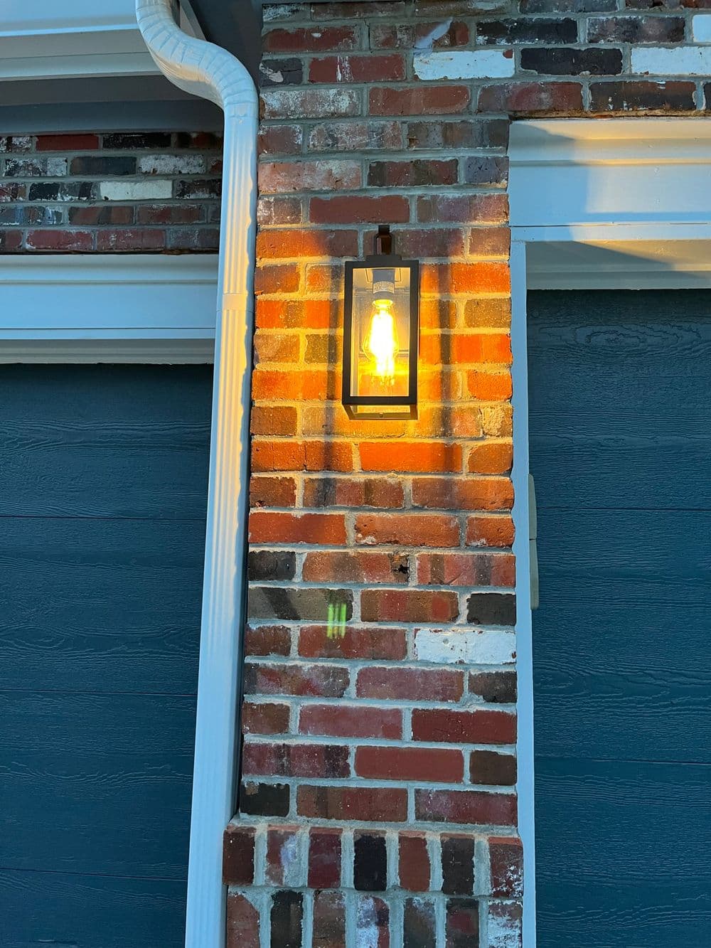 Modern outdoor lantern on brick wall, illuminating dark blue garage doors.