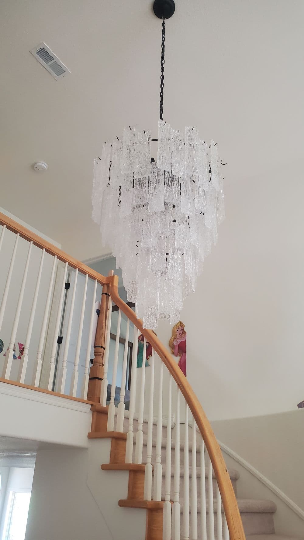 Elegant crystal chandelier hanging from the ceiling above a staircase with wooden railing.