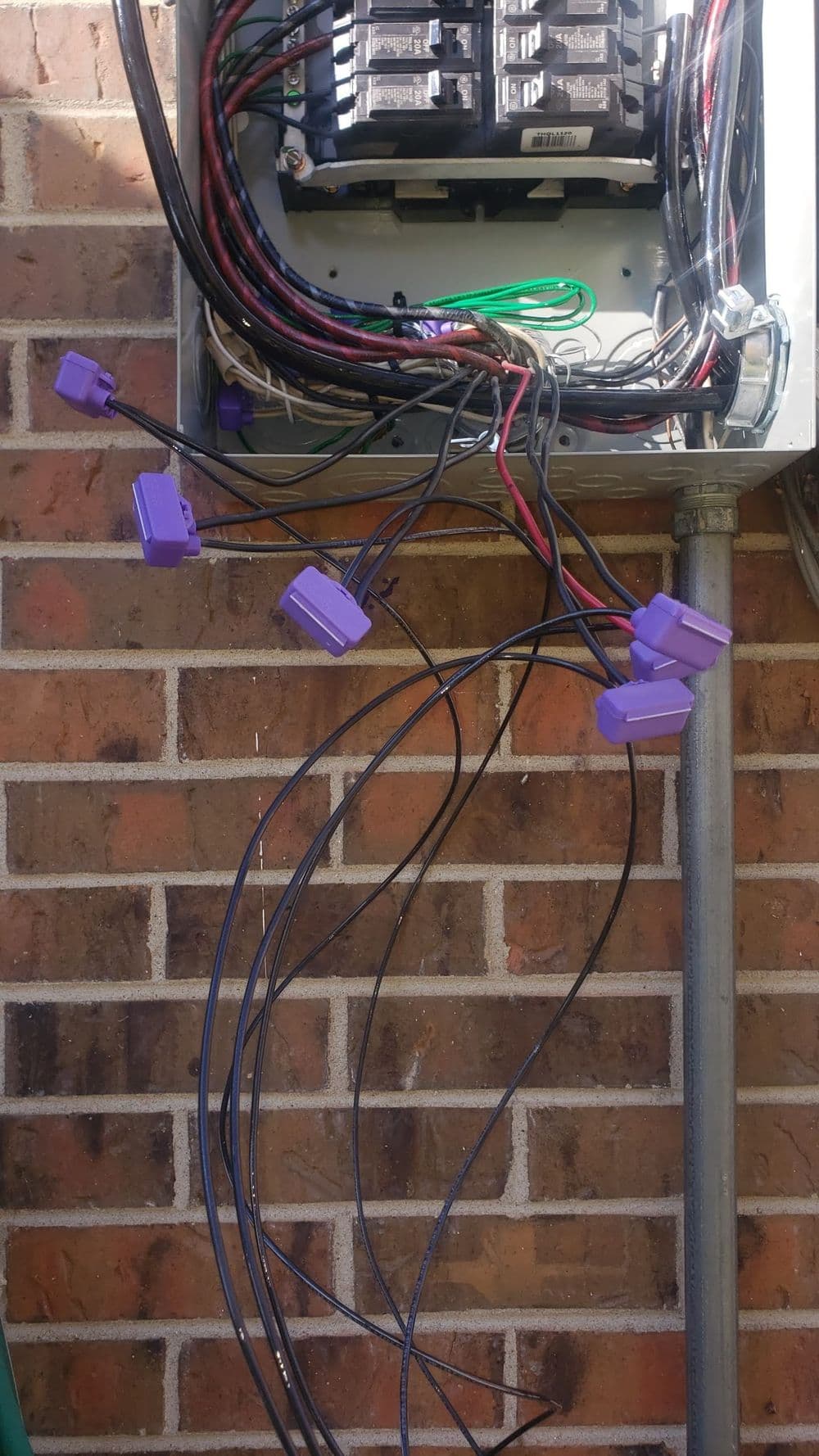 Electrical panel with numerous wires and connectors against a brick wall.