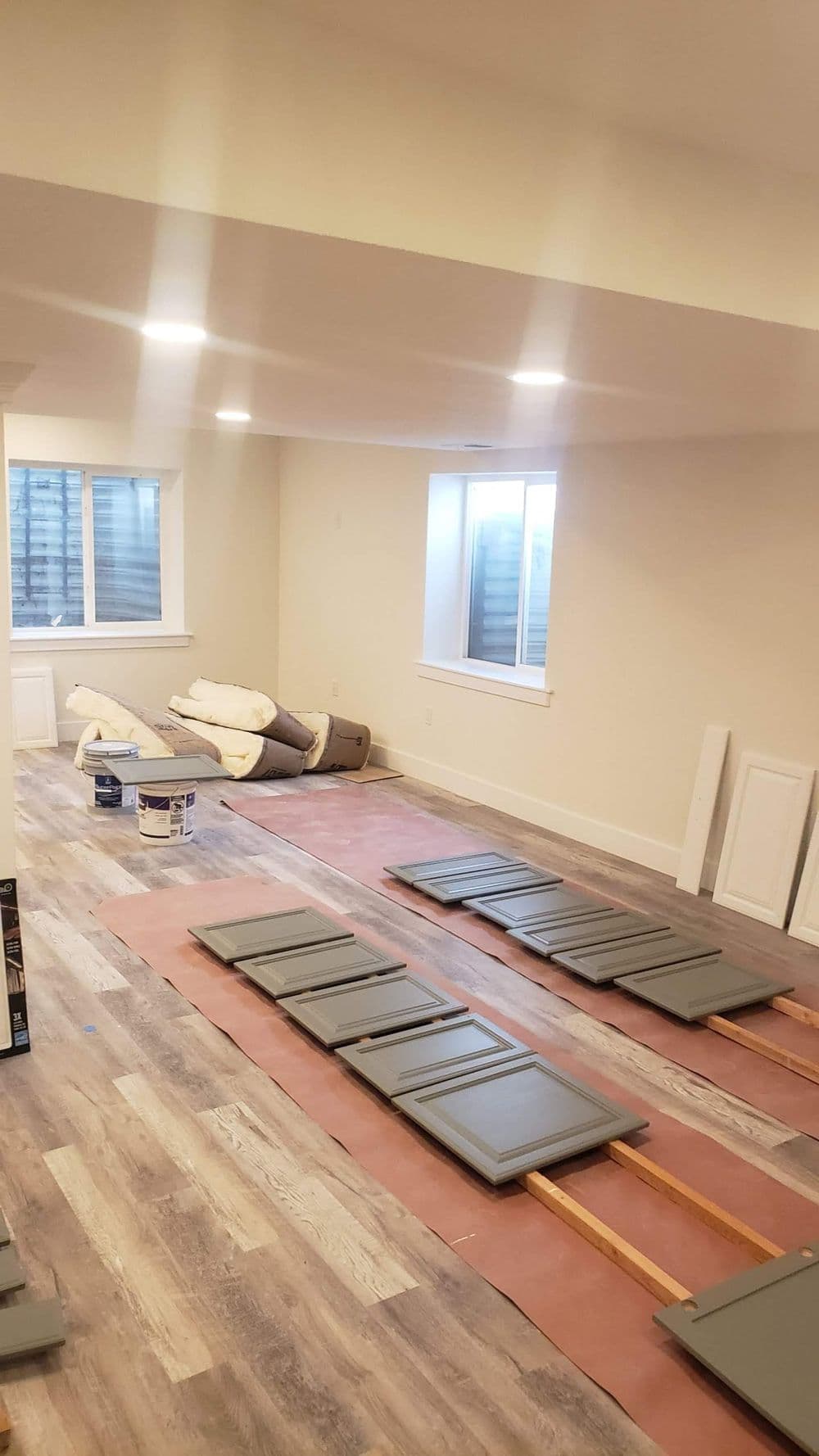 Renovated basement with gray cabinet doors laid out and natural light from windows.