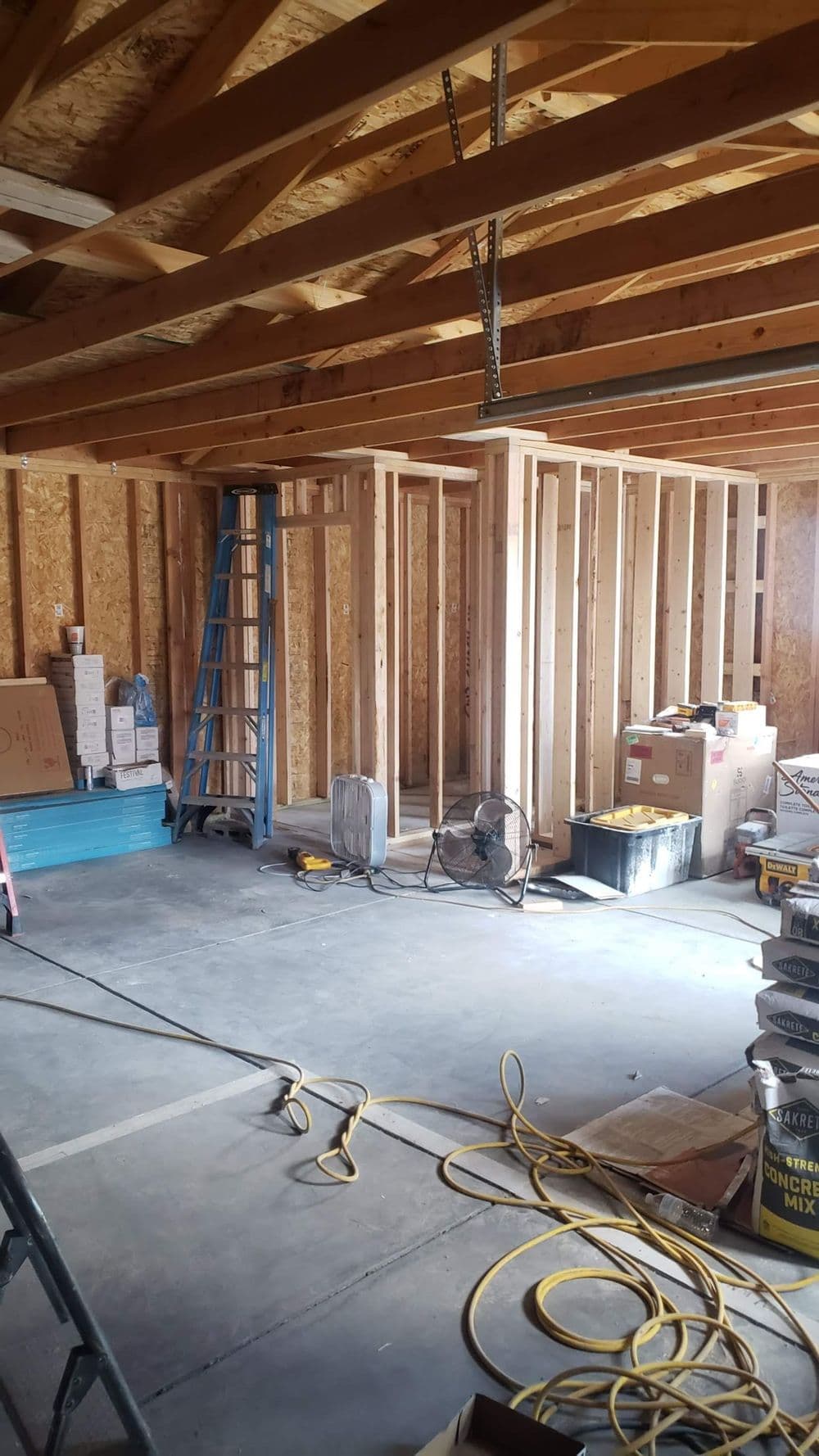 Interior of a garage under construction, with framing, tools, and construction materials visible.