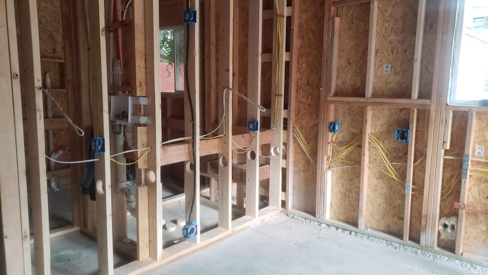 Framed interior of a house under construction with plumbing and electrical wiring visible.