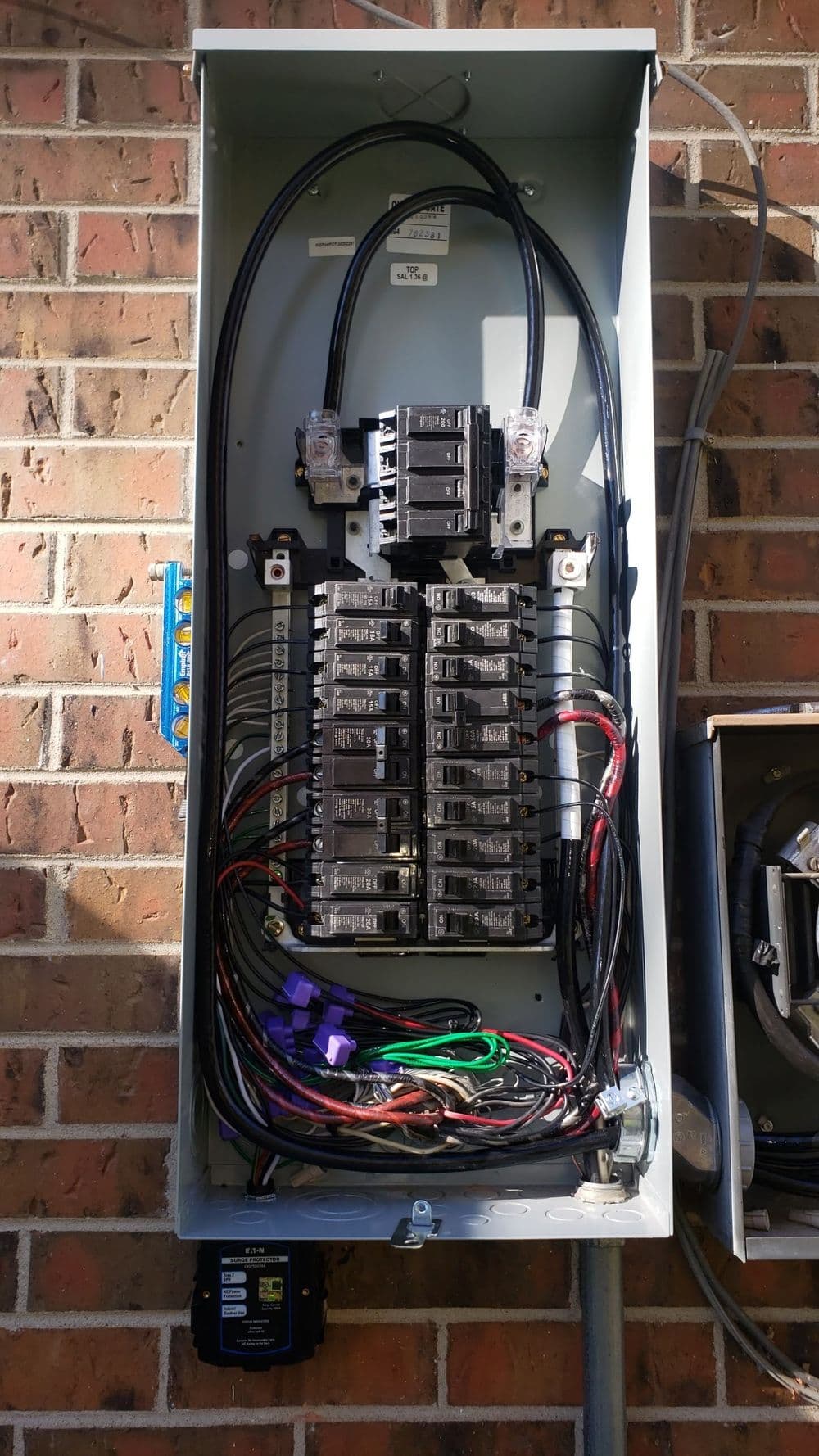 Electrical service panel with circuit breakers and wiring against a brick wall.