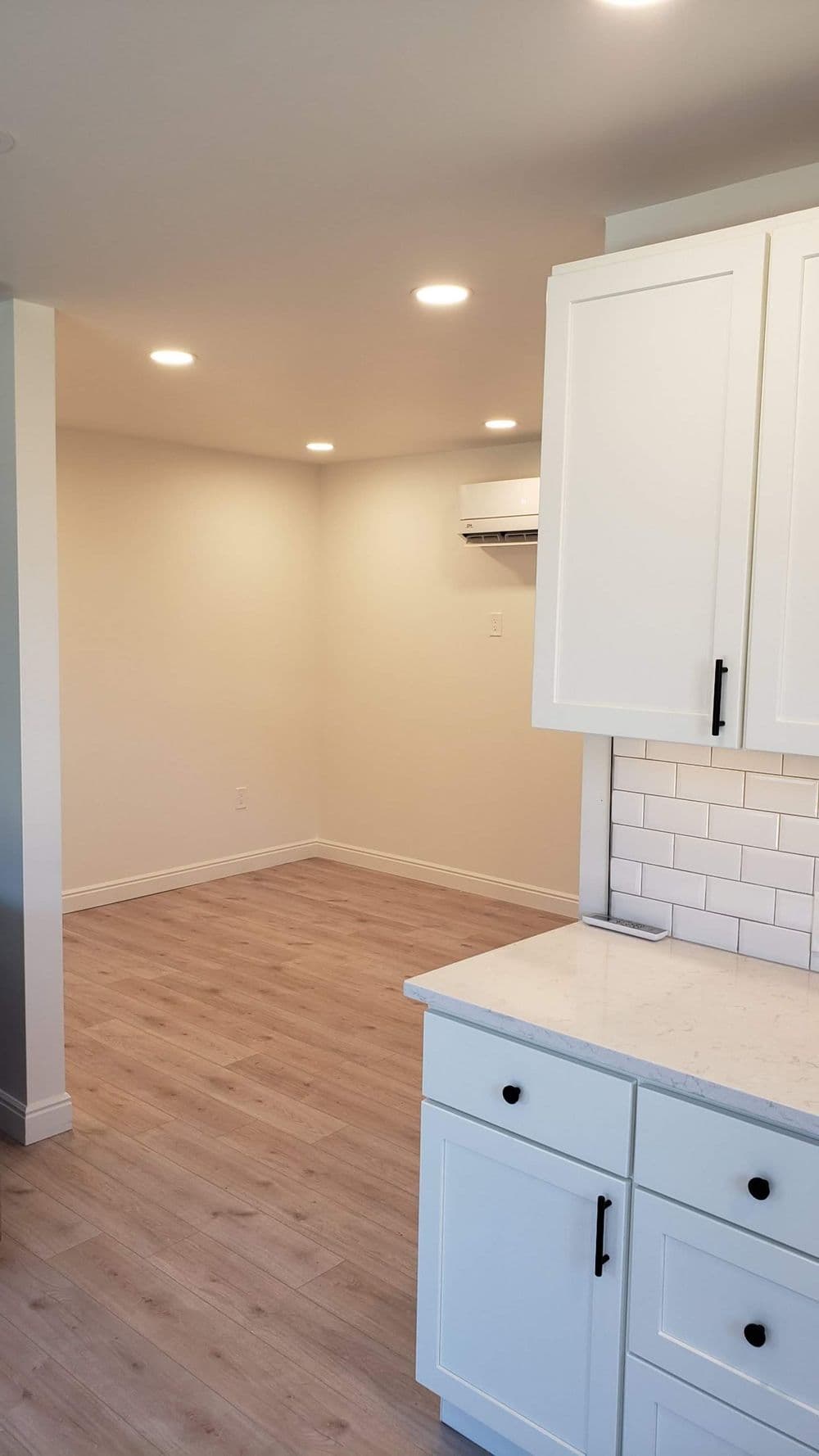 Bright, modern kitchen with white cabinetry and wood flooring, featuring a spacious empty area.