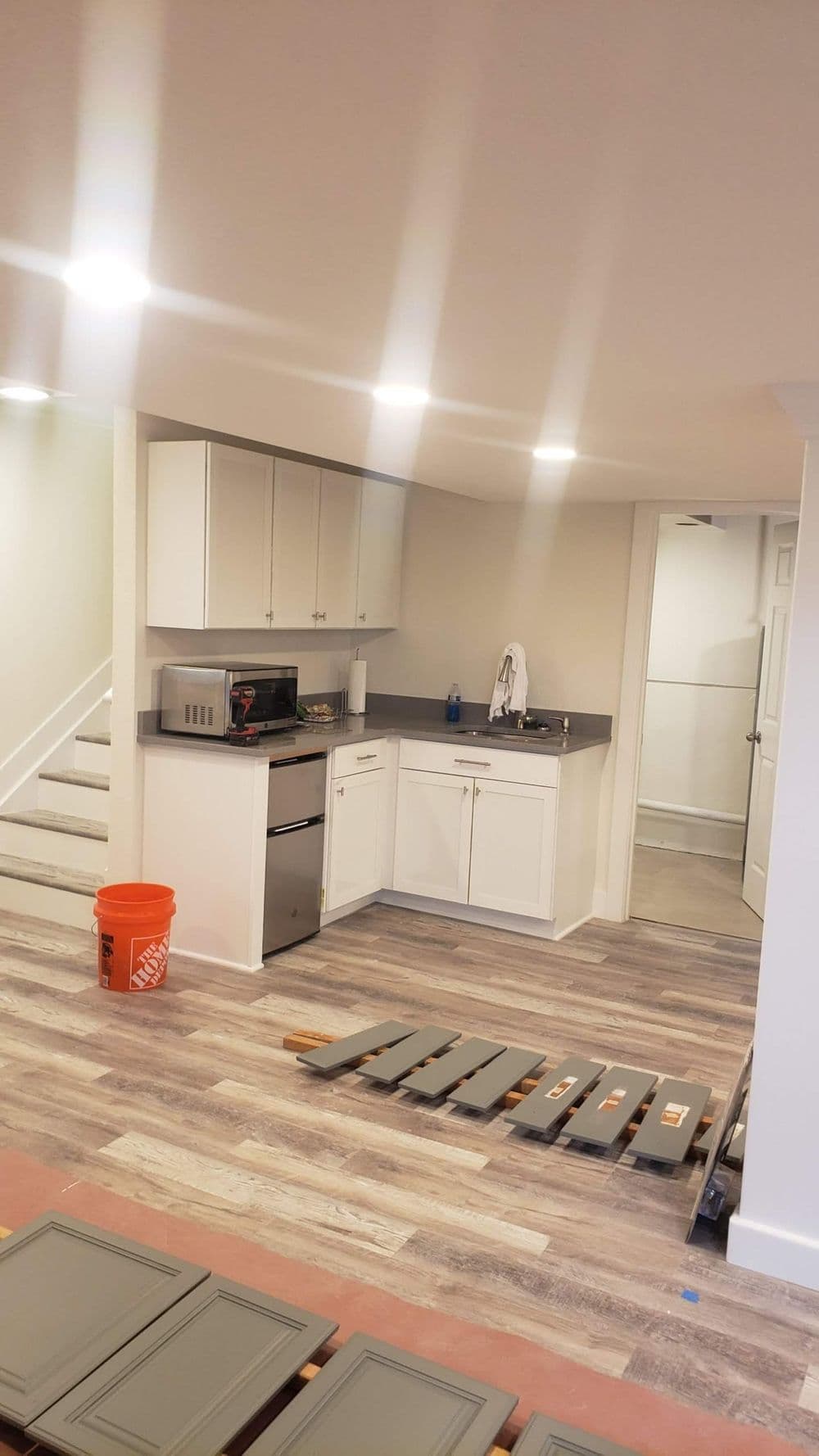 Modern basement kitchen renovation with white cabinets, gray flooring, and staircase.